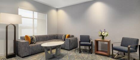 A modern hotel room with a sectional sofa, two armchairs, a small table, and a lamp.