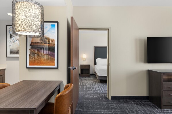 Habitación de hotel con cama, mesita de noche, lámpara, televisor y un área de comedor con mesa y sillas.