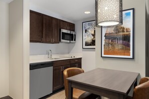 Una cocina moderna con armarios de madera oscura, electrodomésticos de acero inoxidable y una encimera blanca. Hay una mesa de comedor con dos sillas y una lámpara colgante sobre ella.