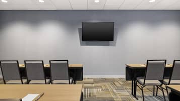 A conference room with a flat-screen TV mounted on the wall, multiple tables with chairs, and a patterned carpet.