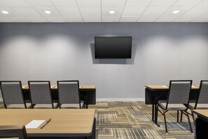 Un salón de conferencias con una pantalla plana montada en la pared, varias mesas con sillas y una alfombra estampada.