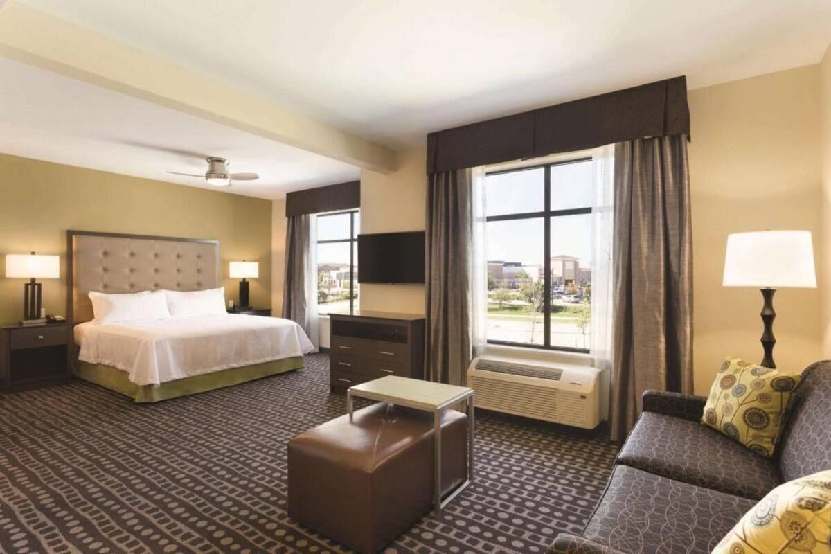 A hotel room with a bed, a sofa, a small table, a TV, and a window with curtains.