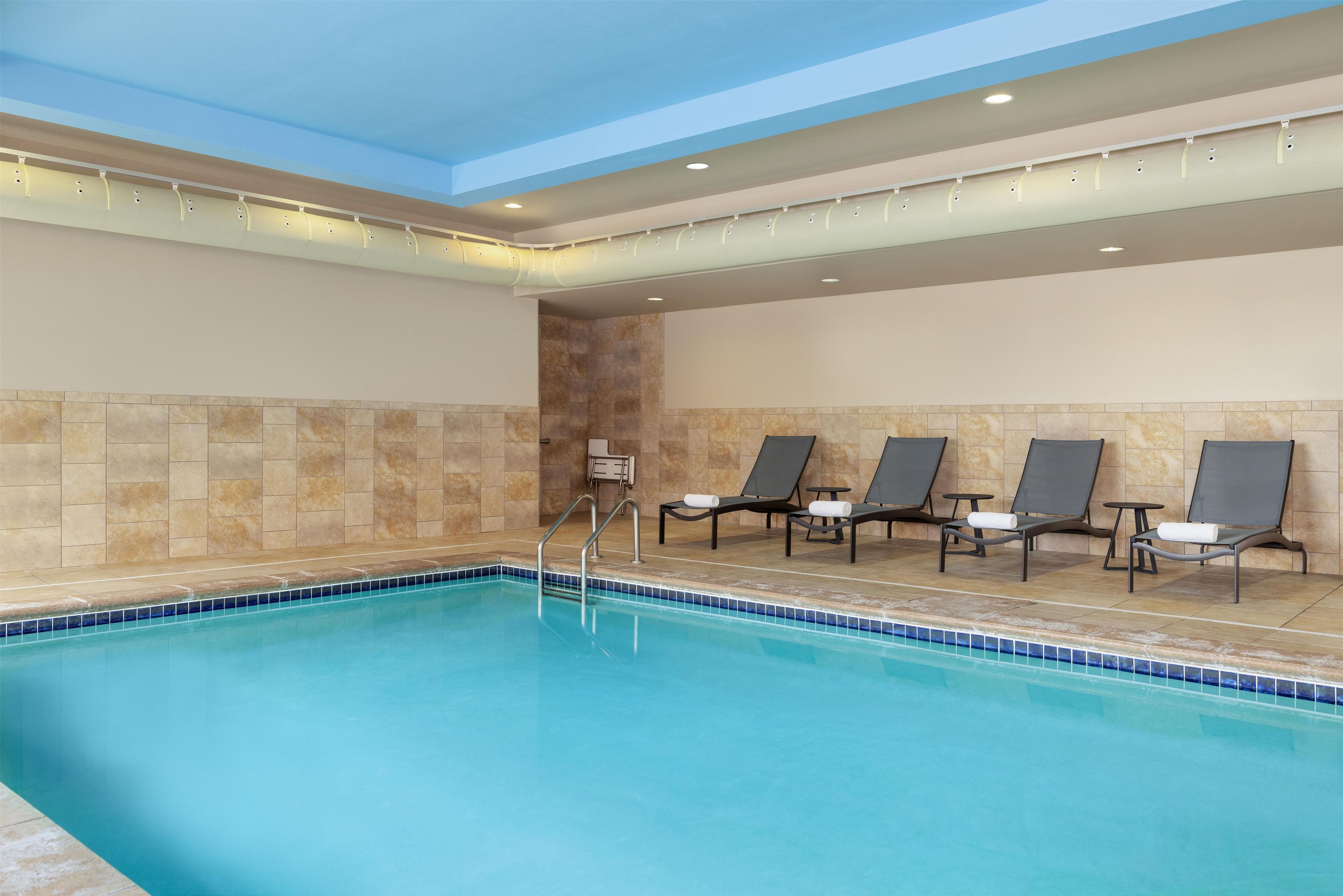 Una piscina con borde de azulejos, rodeada de sillas de descanso con toallas.