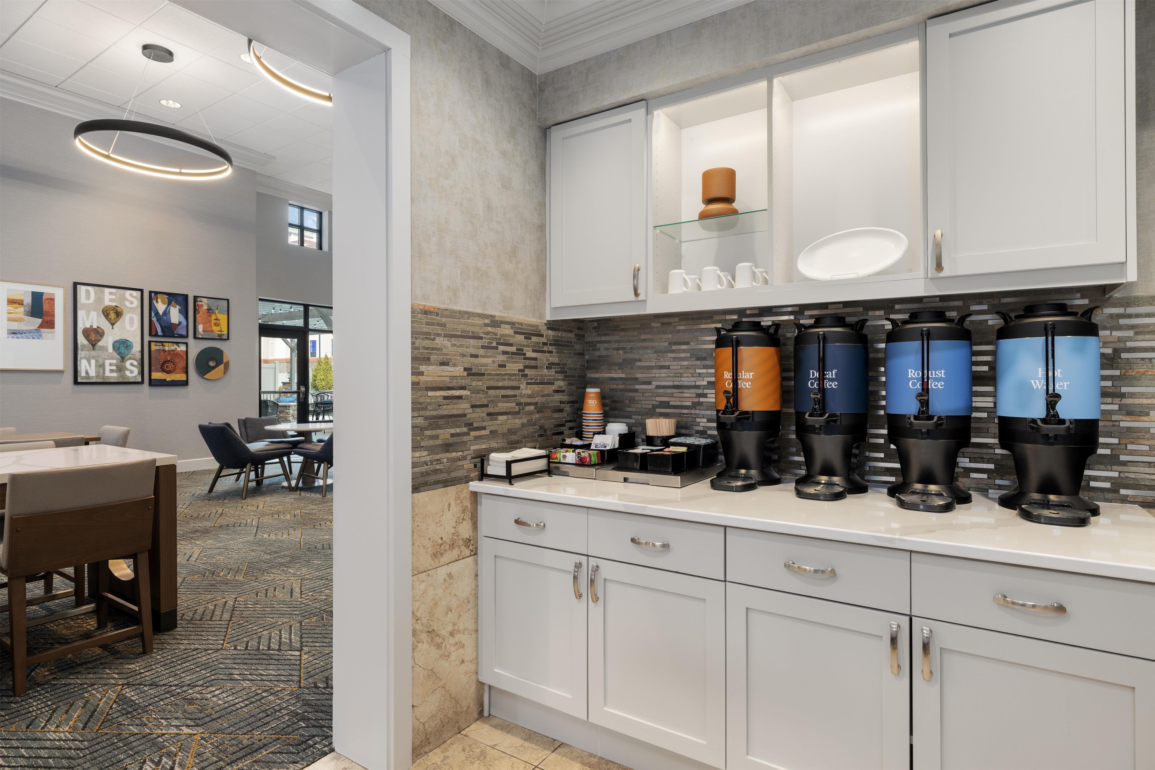 A modern kitchen with built-in coffee machines, a dining area with a patterned rug, and artwork on the walls.