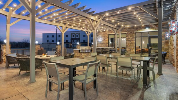Un patio al aire libre con mesas y sillas, una parrilla y una pérgola decorada con luces colgantes.