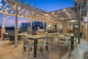 Eine Terrasse im Freien mit Tischen, Stühlen, einem Grill und einer Pergola mit Lichterketten.
