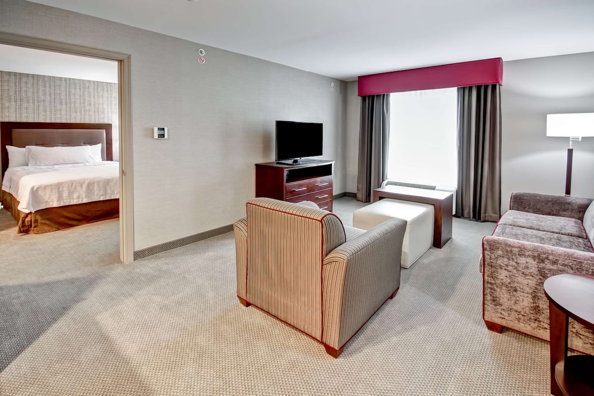 A hotel room with a bed, a TV on a wooden stand, a sofa, a chair, and a desk.