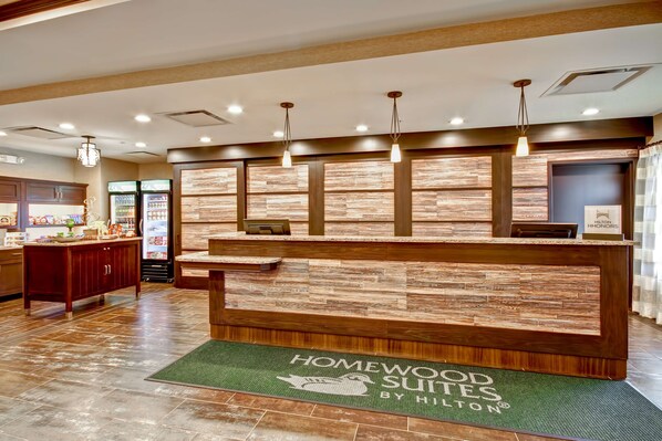 Un mostrador de recepción con diseño de madera y un felpudo verde que dice 'Homewood Suites by Hilton'.