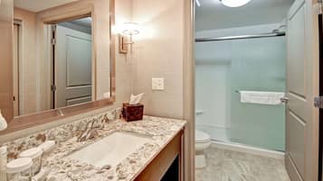 Un baño con lavamanos de mármol, un espejo grande, un perchero y una ducha con mampara de cristal.