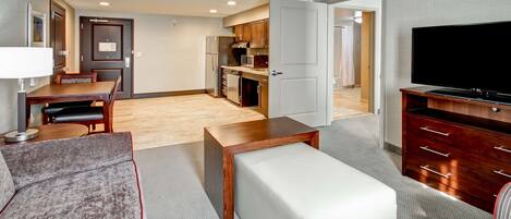 A modern living room with a sofa, a coffee table, a TV stand, and a kitchen in the background.