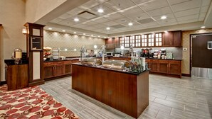 A spacious hotel kitchen with a central island, wooden cabinets, and a patterned carpet. - Homewood Suites by Hilton Bridgewater/Branchburg (Branchburg)