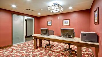 A conference room with a long table, two computer stations, chairs, and framed pictures on the walls.