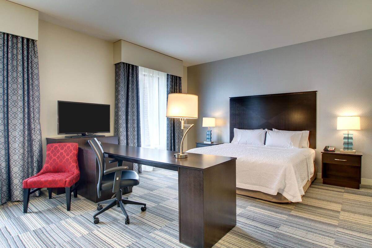 Habitación de hotel con cama, escritorio, silla, televisor y lámparas.