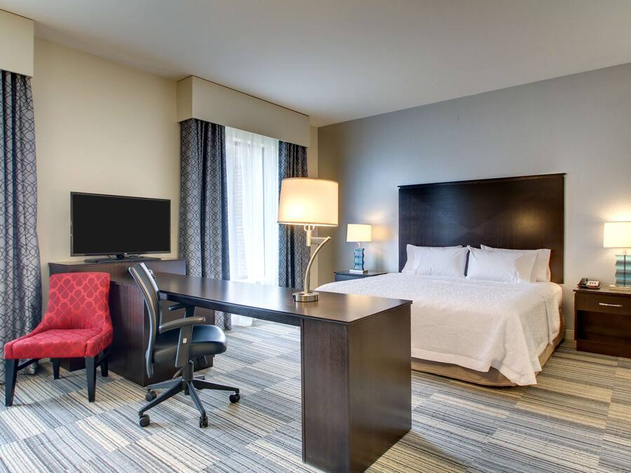 A hotel room with a bed, desk, chair, TV, and lamps.