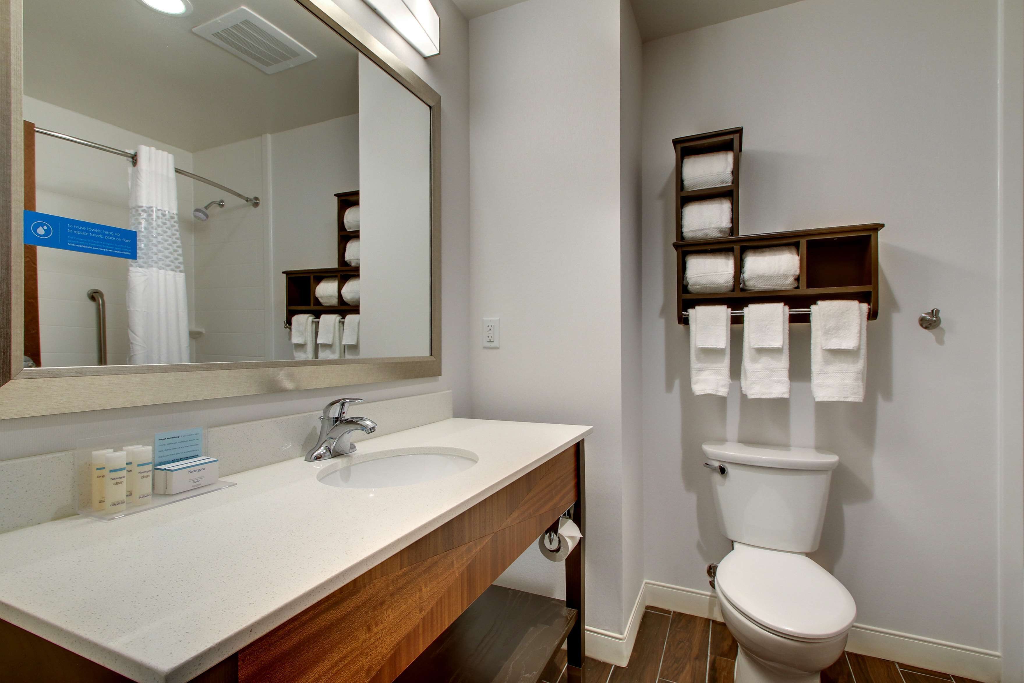 A bathroom with a white sink, mirror, and toilet. There are towels and toiletries on the counter.