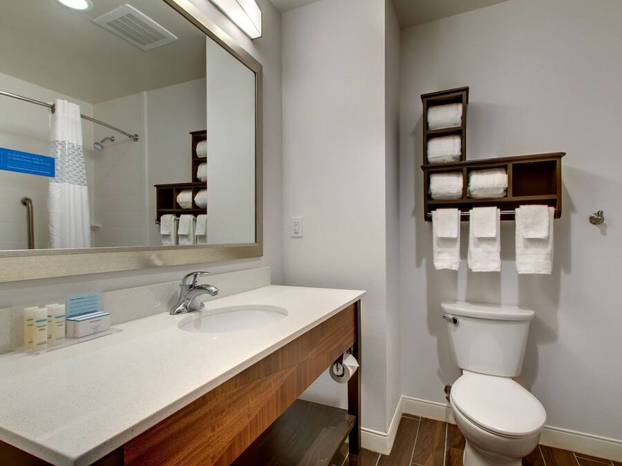 A bathroom with a white sink, mirror, and toilet. There are towels and toiletries on the counter.