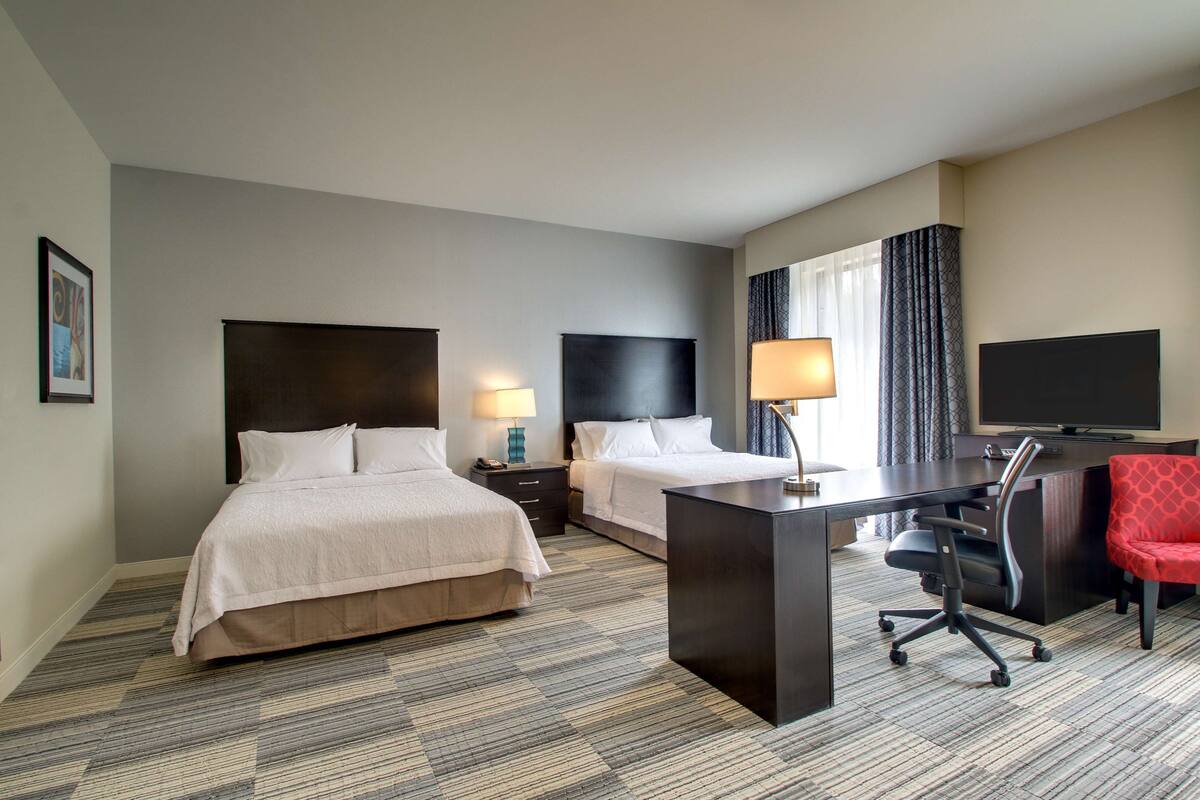 Habitación de hotel con dos camas, un escritorio, una silla, un televisor y una ventana con cortinas.