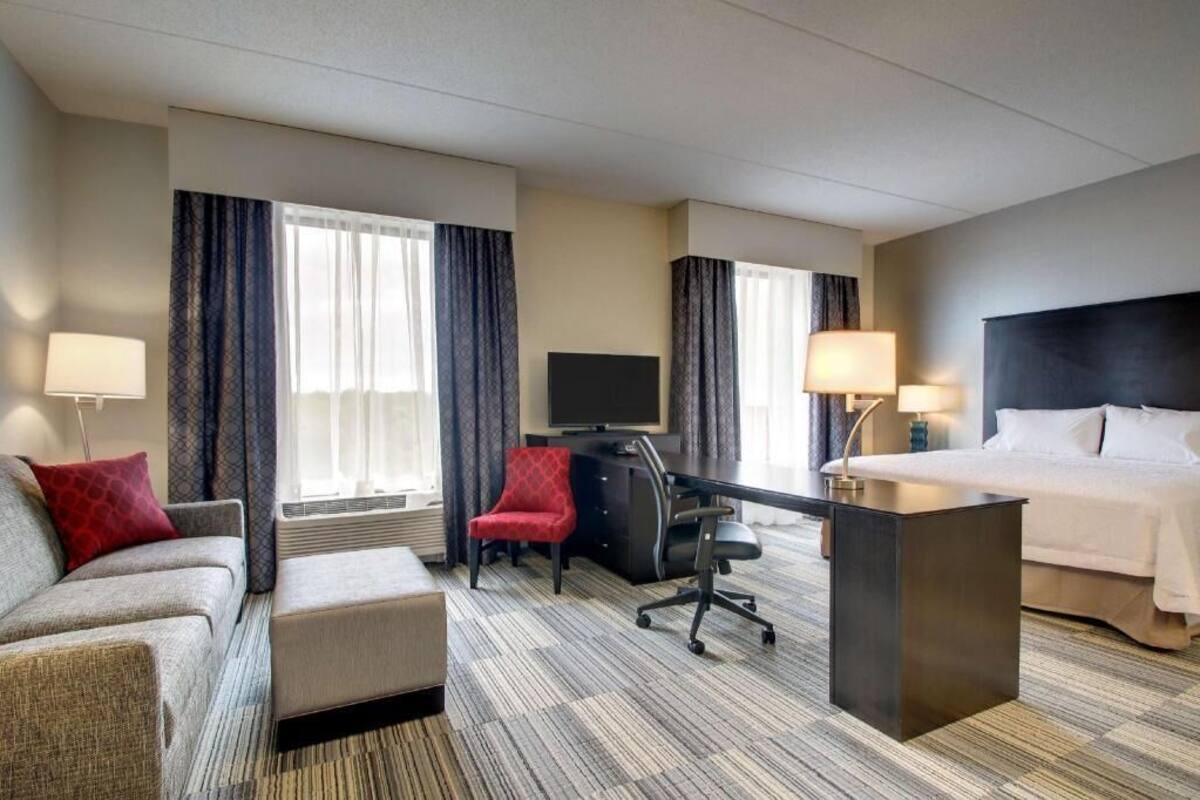 Habitación de hotel con cama, escritorio, computadora, silla, sofá y televisor.