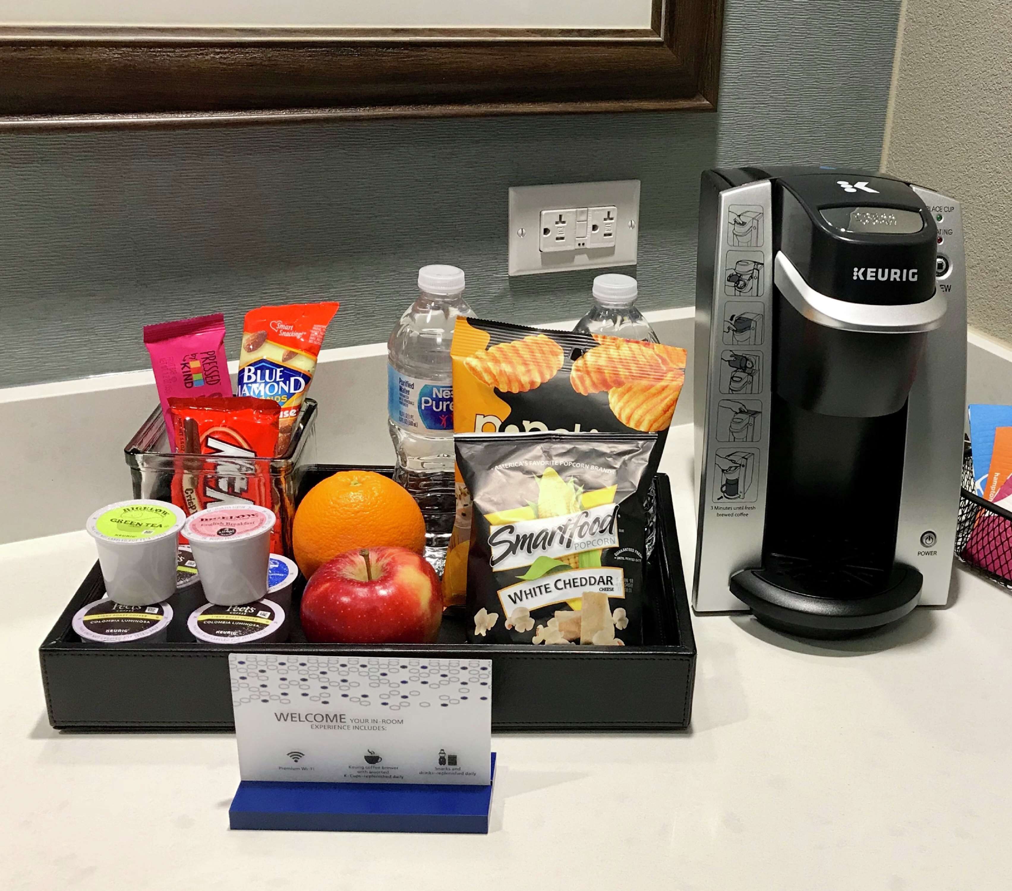 Eine Kaffeemaschine, ein Tablett mit Snacks, eine Wasserflasche und ein Schild, das ein Zimmererlebnis anzeigt.