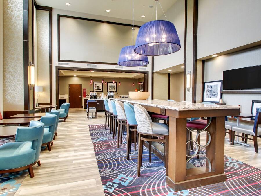 Un vestíbulo de hotel con un mostrador de recepción alargado, varias áreas de descanso y una gran pantalla de televisión.