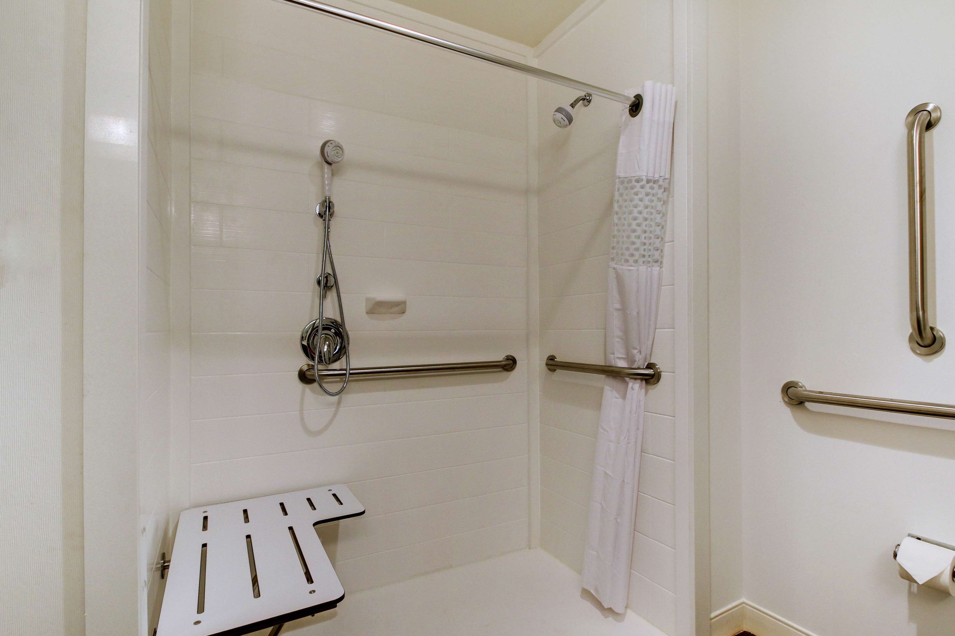 A bathroom with white tiled walls, a shower with a handheld showerhead, a grab bar, and a white towel rack.