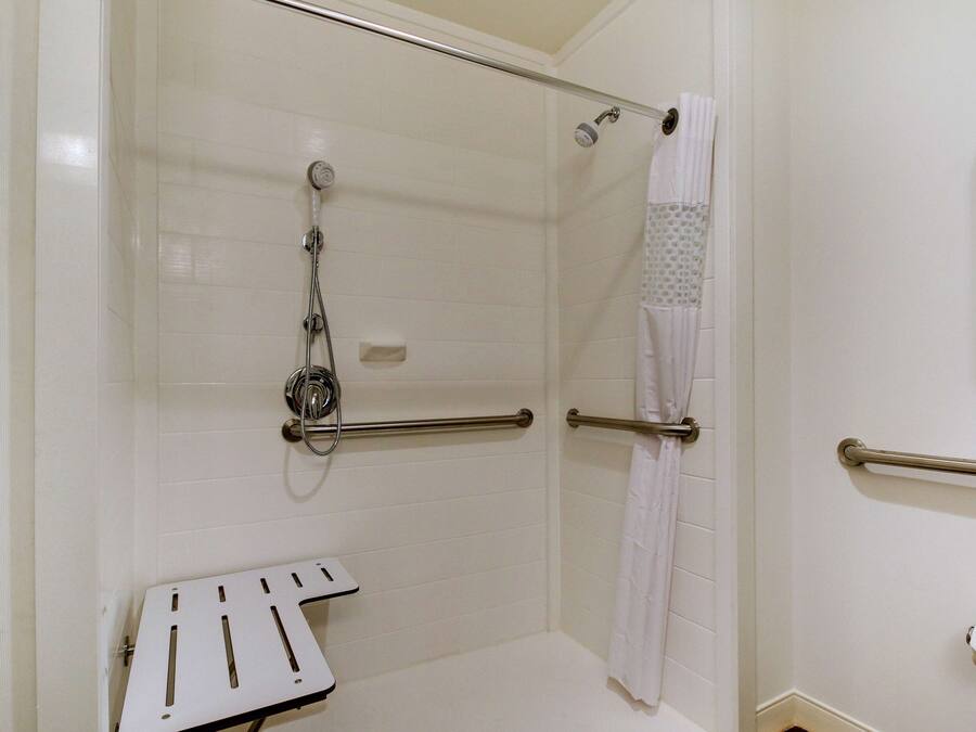 A bathroom with white tiled walls, a shower with a handheld showerhead, a grab bar, and a white towel rack.