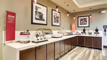 A breakfast bar with a coffee maker, a food warmer, and various breakfast items.