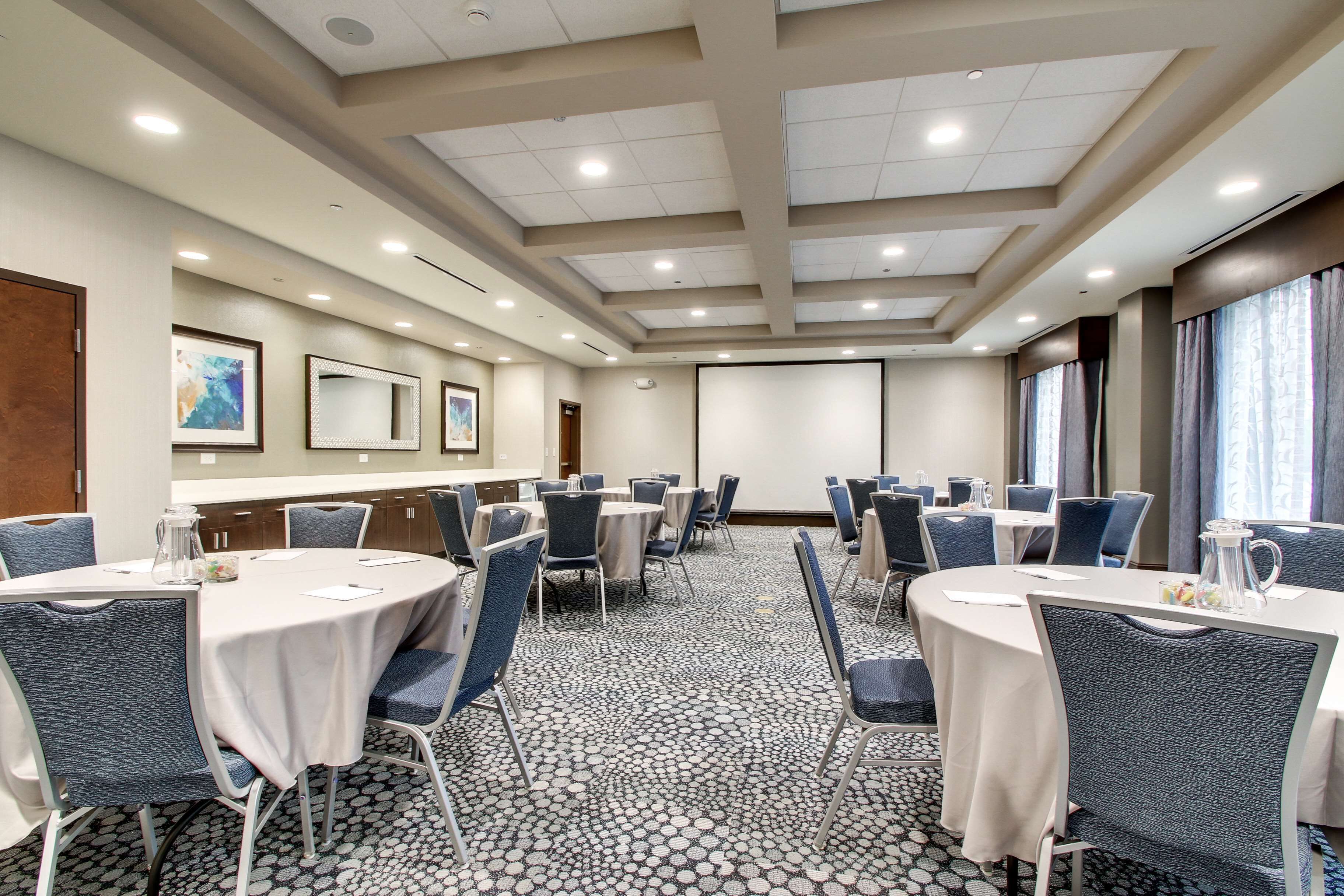 A conference room with round tables, chairs, a projector screen, and a carpeted floor.