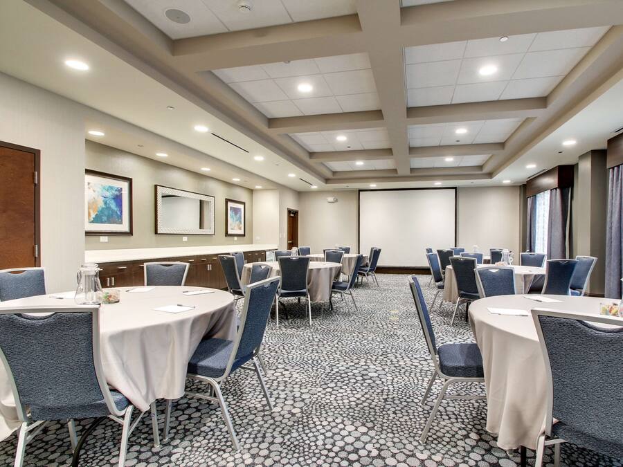 A conference room with round tables, chairs, a projector screen, and a carpeted floor.