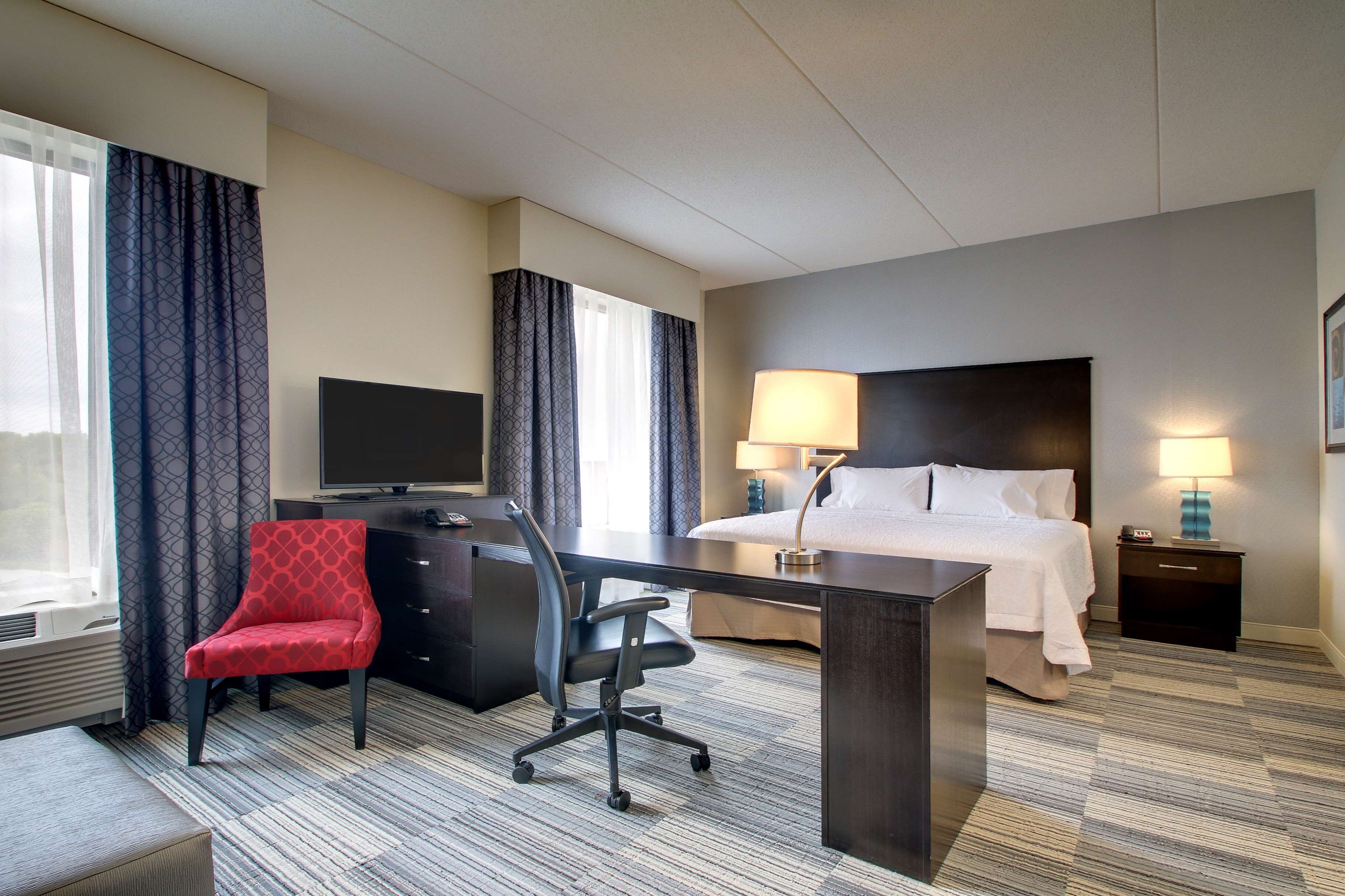 Una habitación de hotel con cama, escritorio, silla, televisor y lámparas.