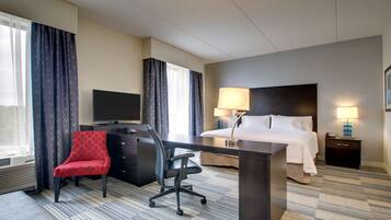 Una habitación de hotel con cama, escritorio, silla, televisor y lámparas.