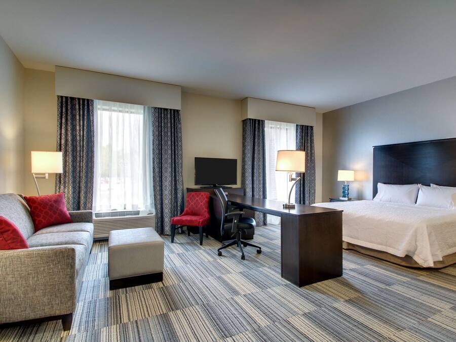 A hotel room with a bed, a desk, a chair, a sofa, and a TV.