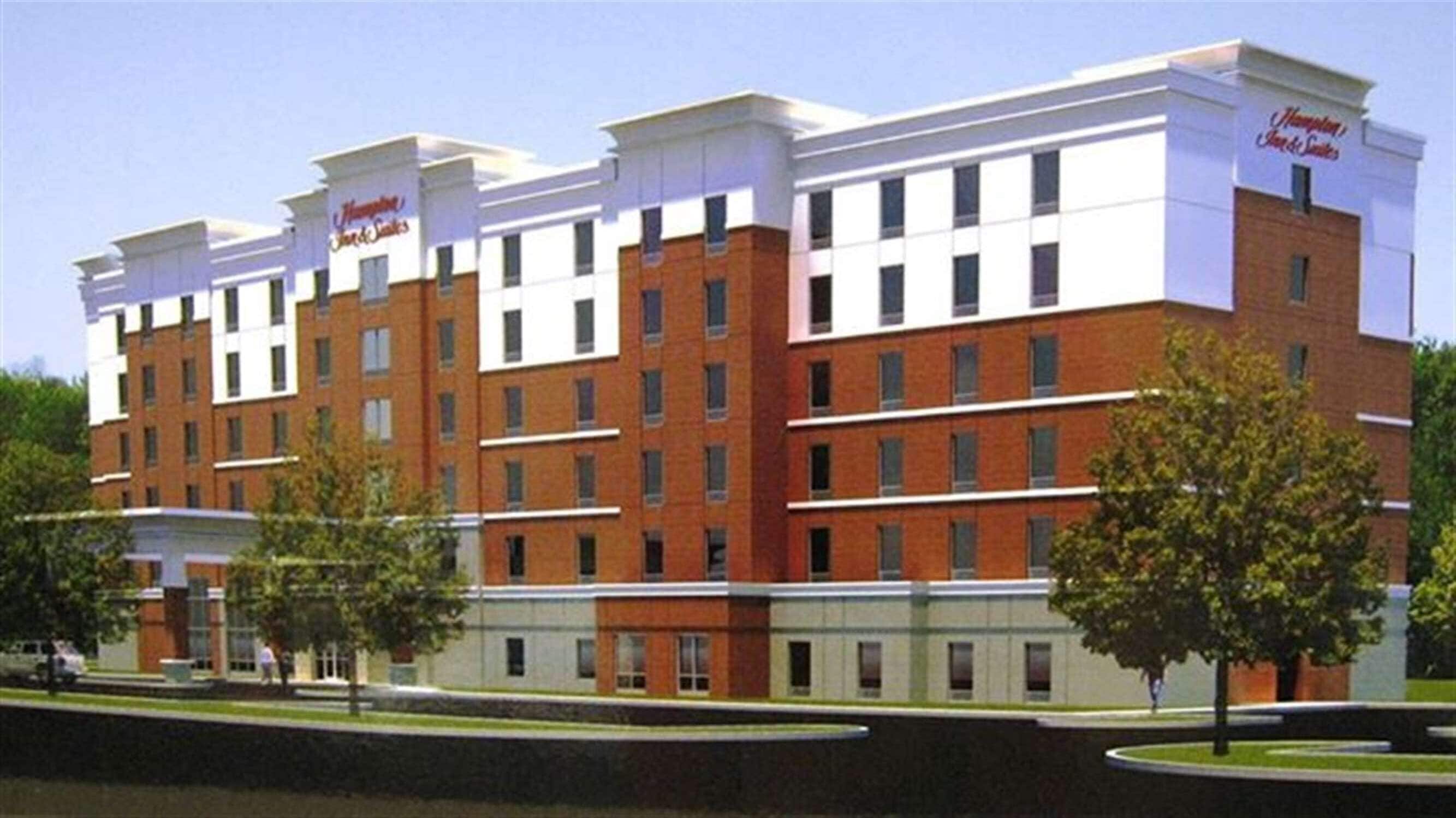 Un hotel de varios pisos con fachada de ladrillo y detalles blancos, que presenta un letrero llamativo de Hampton Inn & Suites.