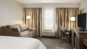 A hotel room with a bed, a sofa, a desk with a TV, a chair, and a window with curtains. - Hampton Inn & Suites Minooka (Minooka)
