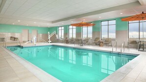 An indoor swimming pool with clear blue water, surrounded by lounge chairs and tables, and large windows offering a view. - Hampton Inn & Suites Minooka (Minooka)