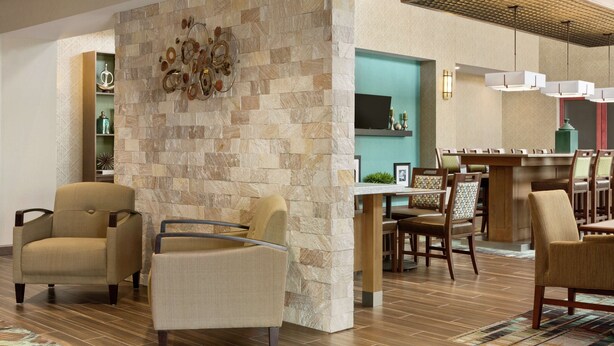 A lobby with a stone wall, seating area, and a reception desk. - Hampton Inn & Suites Minooka (Minooka)