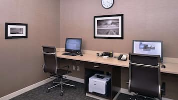 Un bureau d’hôtel avec deux bureaux, des ordinateurs, des chaises, une horloge et des tableaux encadrés accrochés au mur.