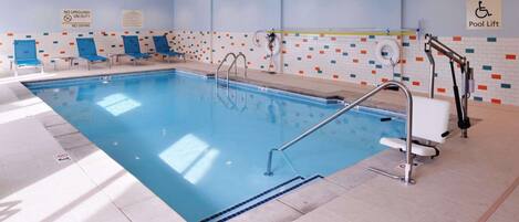 Piscina interior com água azul, elevador de piscina e placa de proibição de mergulho.
