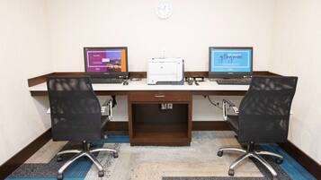 A conference room with two desks, each with a laptop, a printer, and a chair.