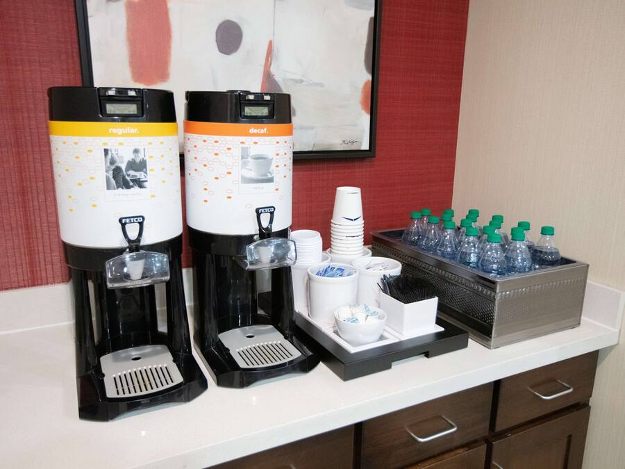 Una estación de café con dos máquinas de café, vasos desechables y un dispensador de agua.