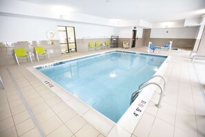Ein Hallenbad mit klarem Wasser, einem Sprungbrett und mehreren Liegestühlen.
