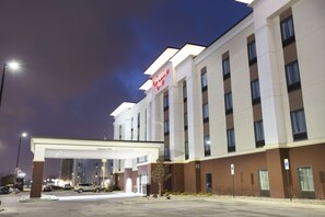 Ein Hampton Inn Hotel bei klarer Nacht, mit gut beleuchtetem Eingang und Parkplatz mit Autos.