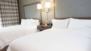 A hotel room with two beds, a nightstand with a lamp, and a mirror.