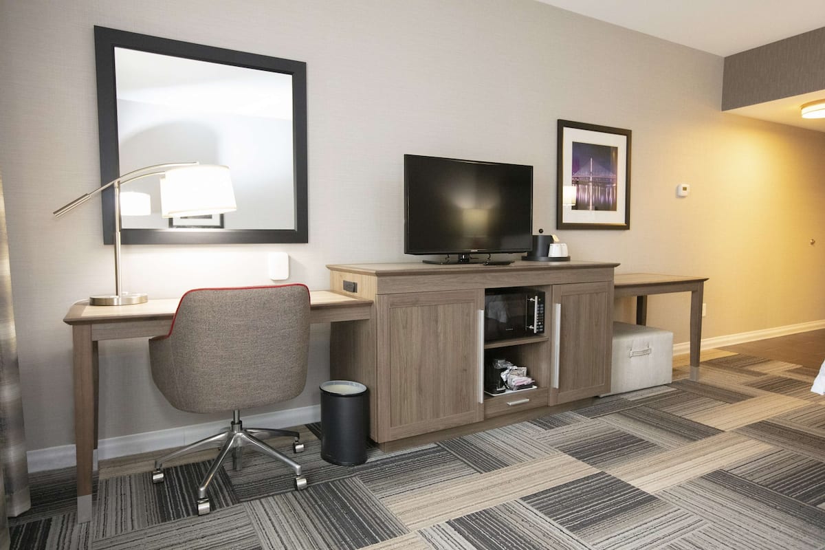 Quarto de hotel com escrivaninha, cadeira, TV e um quadro na parede.