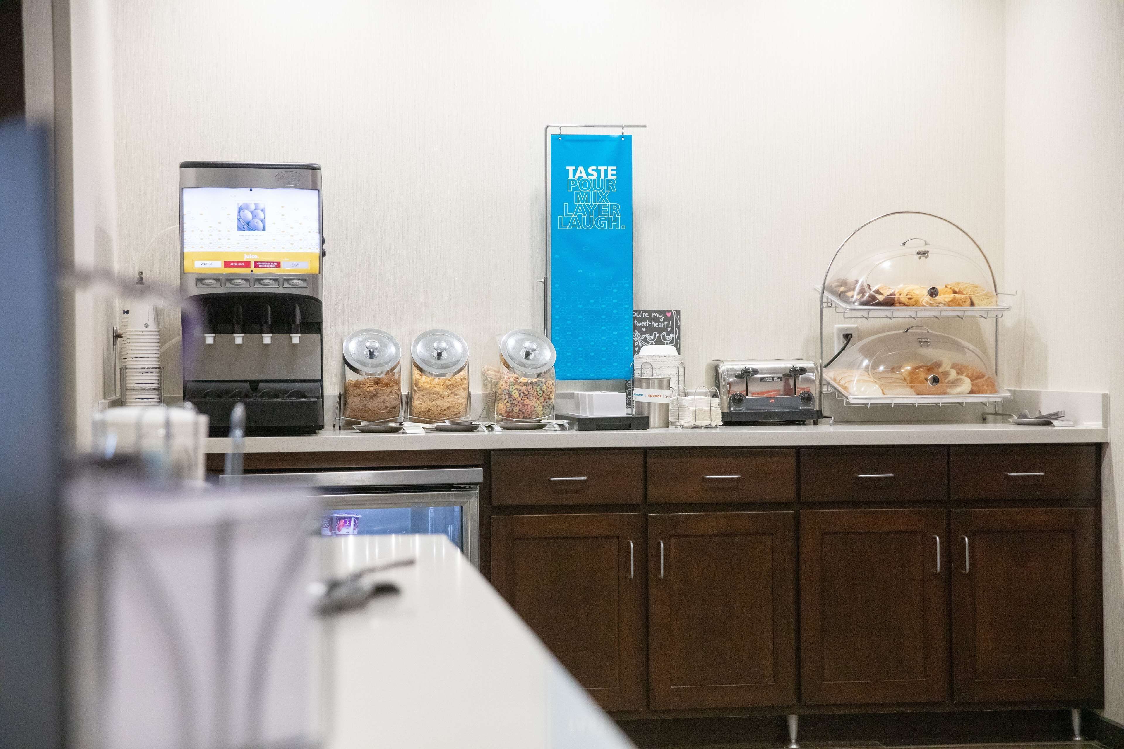 A breakfast bar with a coffee machine, a beverage dispenser, and a display of pastries and cereals.