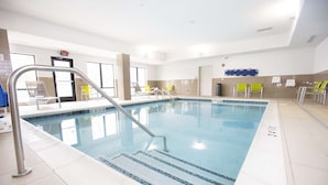 Una piscina interior con agua cristalina, una escalera metálica y sillas amarillas alrededor del borde.