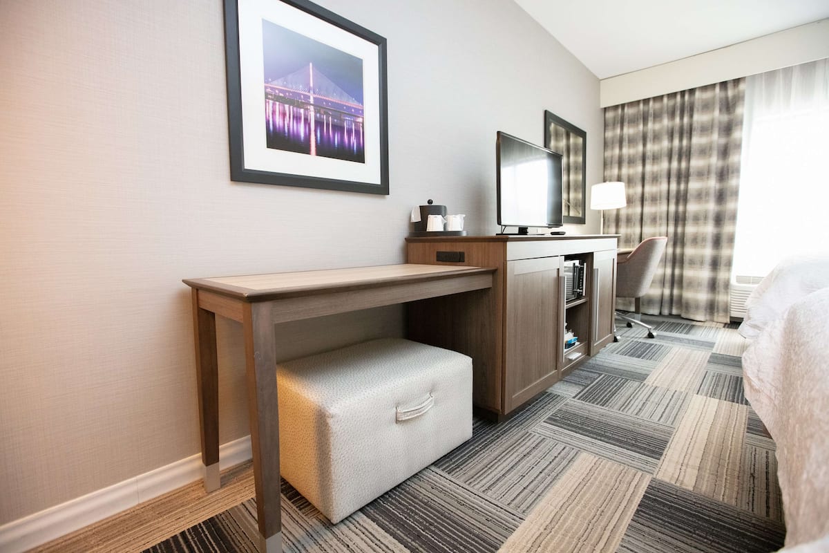 Quarto de hotel com escrivaninha, cadeira, cama, televisão e quadro de uma ponte na parede.