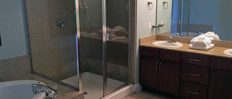 Un baño moderno con ducha envuelta en vidrio, bañera y tocador con lavabo y espejo.
