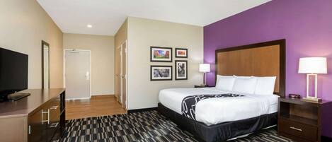 Una habitación de hotel con cama, escritorio, televisor y puerta.