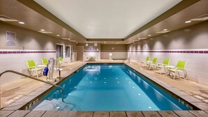 Una piscina interior con carriles delimitados, sillas verdes a los lados y una pared de azulejos con un letrero.